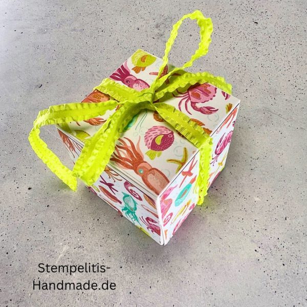 Handdekorierte Geschenkschachtel mit Schleife von oben, Geschenkschachtel mit liebevollem Aufkleber “Mit viel Liebe verschenkt”, Detailansicht Schleife auf Geschenkschachtel, Seitenansicht Geschenkschachtel mit buntem Designpapier, Offene Geschenkbox zum Befüllen, Geschenkschachtel auf hellem Hintergrund mit Dekorband, Handgemachte Geschenkverpackung mit grünem Band und Etikett